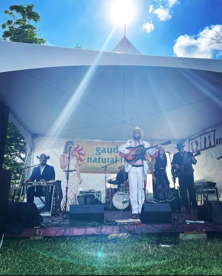 The Handsome Devils performing live on stage under a white tent at the Mariposa Folk Festival